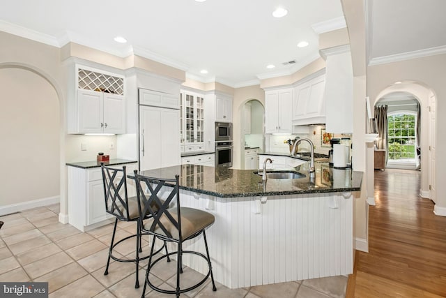 kitchen with arched walkways, appliances with stainless steel finishes, a sink, a peninsula, and white cabinetry