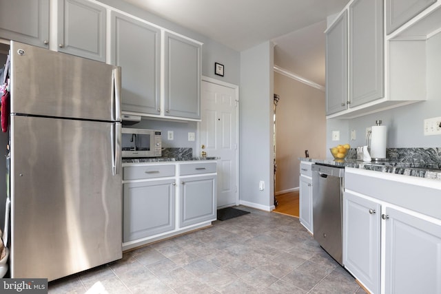 kitchen featuring appliances with stainless steel finishes, baseboards, stone finish flooring, and dark stone countertops