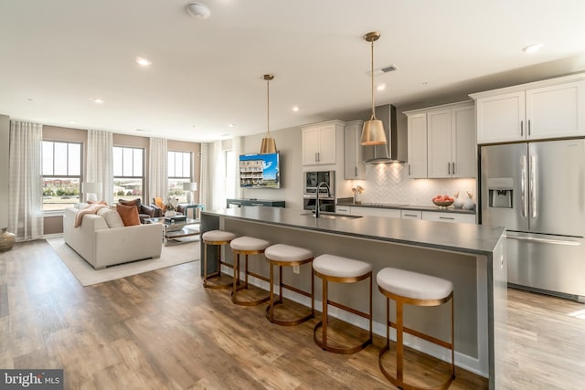 kitchen featuring stainless steel appliances, wall chimney range hood, a sink, dark countertops, and a breakfast bar area