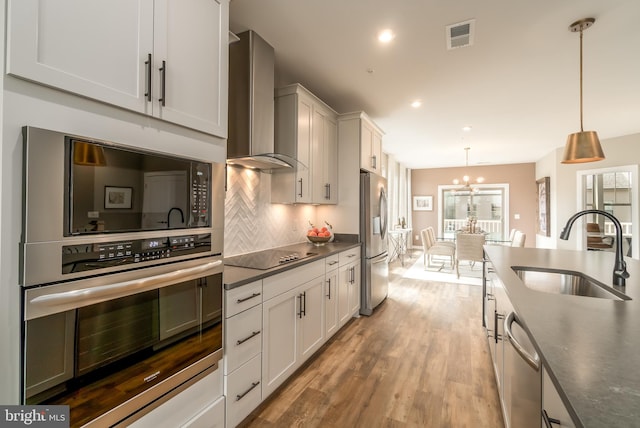 kitchen featuring appliances with stainless steel finishes, wall chimney range hood, a sink, dark countertops, and a chandelier
