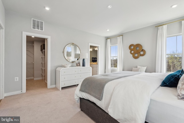 bedroom featuring a walk in closet, light colored carpet, recessed lighting, baseboards, and ensuite bath