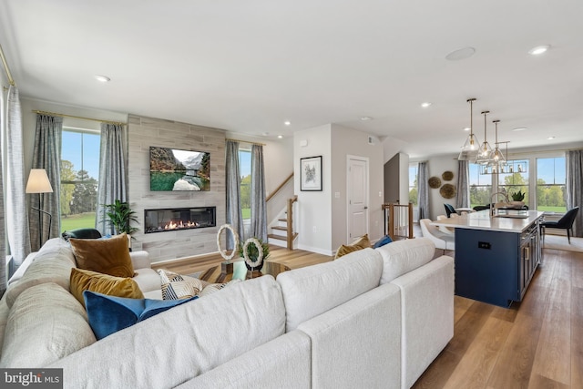 living area with a large fireplace, baseboards, recessed lighting, light wood-style floors, and stairs