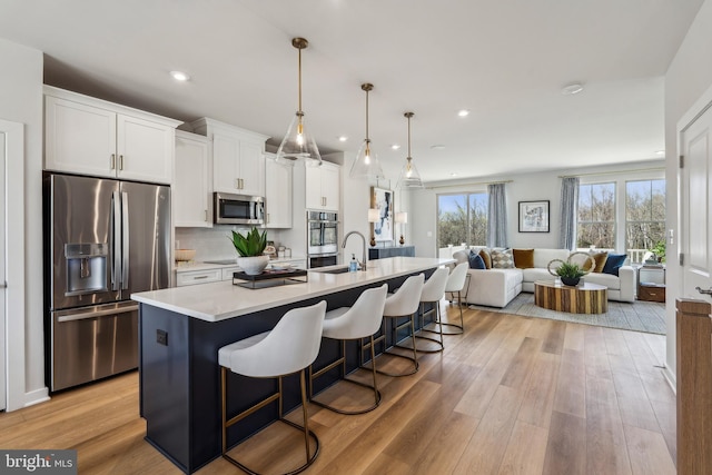 kitchen featuring appliances with stainless steel finishes, a kitchen bar, a center island with sink, open floor plan, and white cabinets