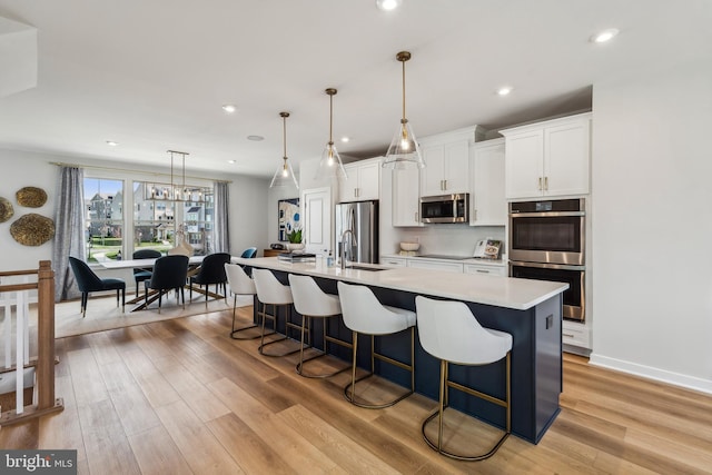 kitchen with stainless steel appliances, an island with sink, light countertops, light wood-type flooring, and a kitchen breakfast bar