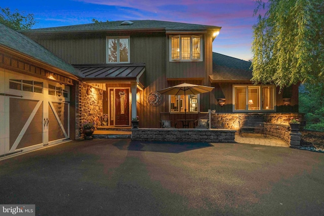 3097 Mill Rd, Doylestown, PA 18902 - back of property at dusk featuring a standing seam roof, stone siding, a shingled roof, metal roof, and a garage