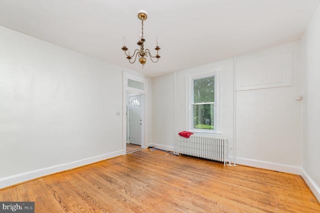 spare room with radiator, a chandelier, baseboards, and light wood finished floors