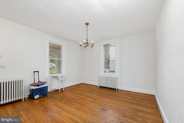 unfurnished room with radiator heating unit, a chandelier, wood finished floors, and baseboards