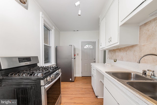 kitchen with appliances with stainless steel finishes, a sink, white cabinets, light wood-style floors, and light countertops
