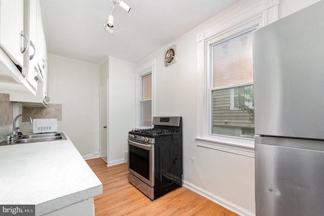 kitchen featuring stainless steel appliances, a sink, light wood-type flooring, light countertops, and ornamental molding