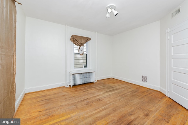 unfurnished room with radiator heating unit, light wood-type flooring, and baseboards