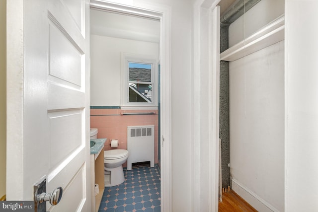half bathroom featuring radiator, toilet, tile walls, vanity, and wainscoting