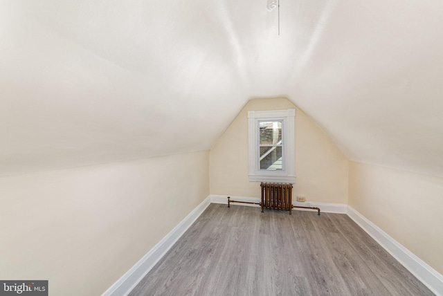 additional living space with wood finished floors, radiator, lofted ceiling, and baseboards