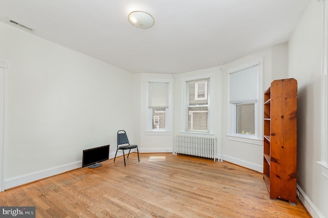 unfurnished room featuring radiator heating unit, light wood-style floors, and baseboards