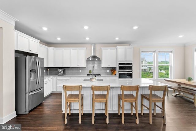 19253 Running Spring Ct, Leesburg, VA 20175 - kitchen featuring appliances with stainless steel finishes, wall chimney exhaust hood, decorative backsplash, white cabinets, and an island with sink