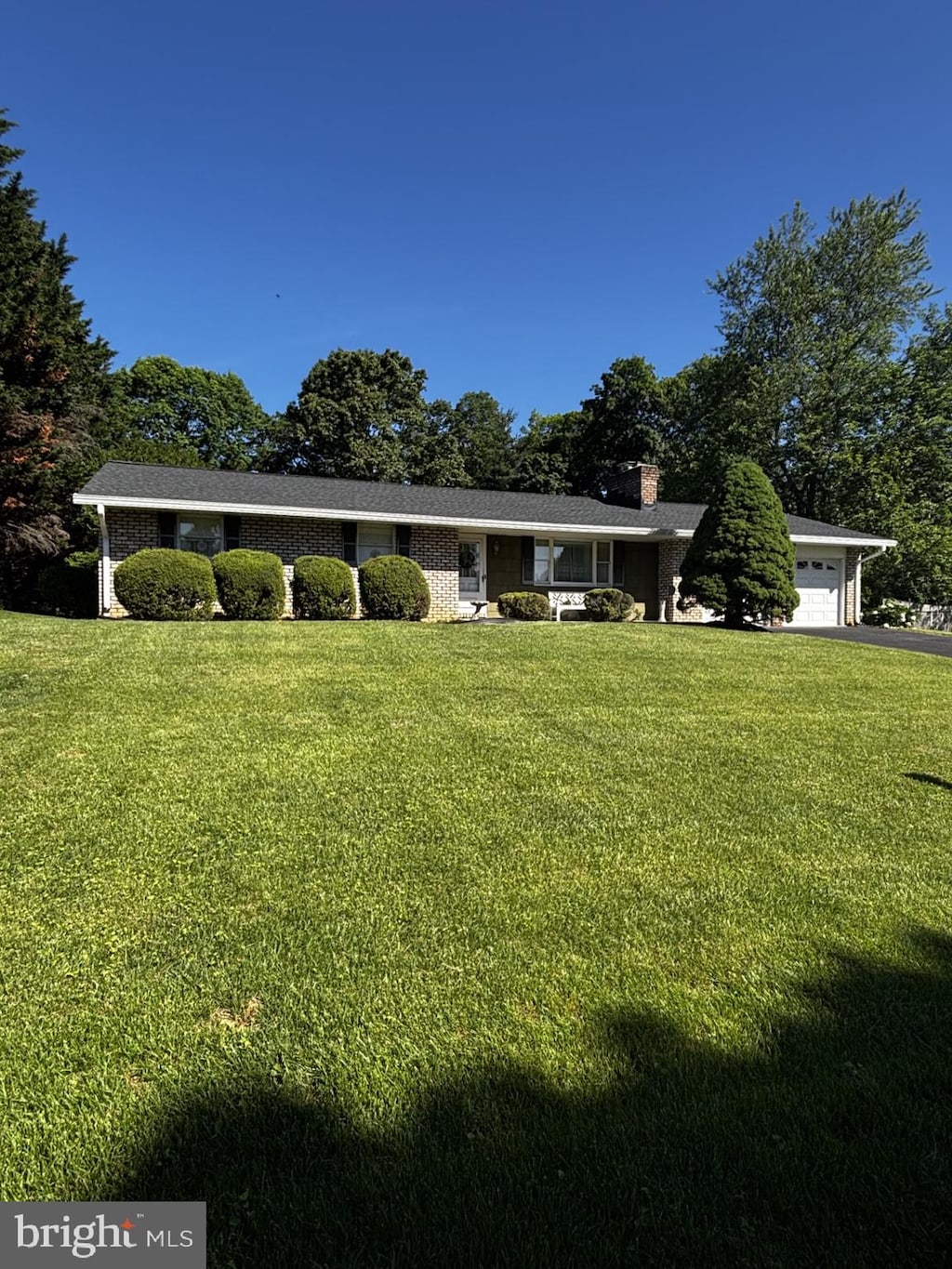 ranch-style house featuring a garage, a chimney, a front yard, and driveway