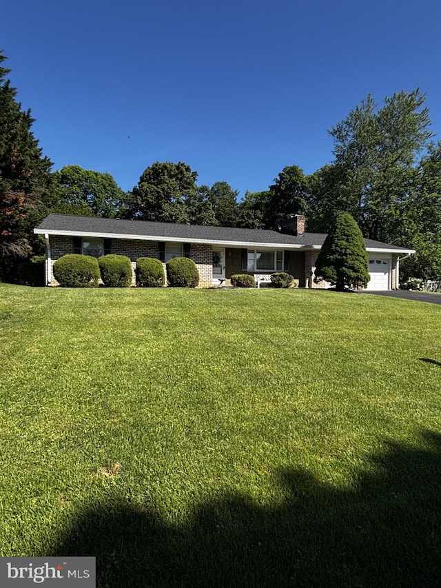 ranch-style house featuring a garage, a chimney, a front yard, and driveway