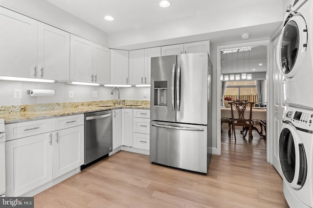 7374 Park Heights Ave, Baltimore, MD 21208 - kitchen featuring stainless steel appliances, stacked washing machine and dryer, a sink, white cabinetry, and light wood-type flooring