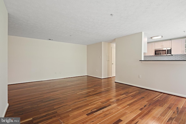 unfurnished living room featuring hardwood / wood-style floors, a textured ceiling, and baseboards