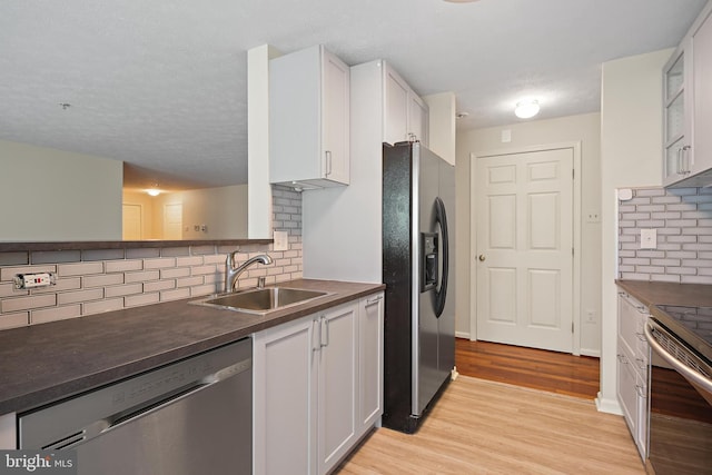 kitchen featuring stainless steel appliances, dark countertops, a sink, light wood-style flooring, and white cabinets