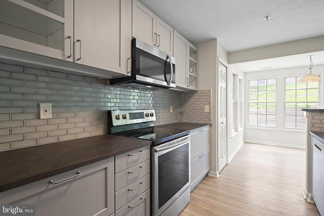 kitchen with stainless steel appliances, dark countertops, light wood-style floors, baseboards, and a textured ceiling