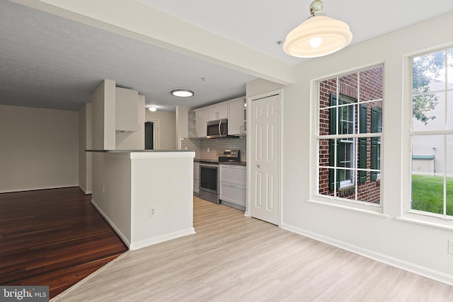 kitchen with appliances with stainless steel finishes, light wood-type flooring, tasteful backsplash, white cabinetry, and baseboards