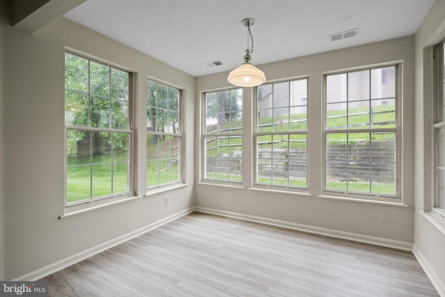unfurnished sunroom featuring healthy amount of natural light, wood finished floors, and baseboards