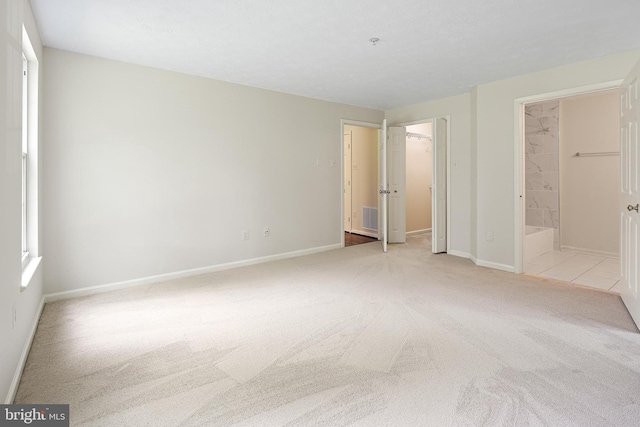unfurnished bedroom with carpet flooring, baseboards, a walk in closet, connected bathroom, and a closet