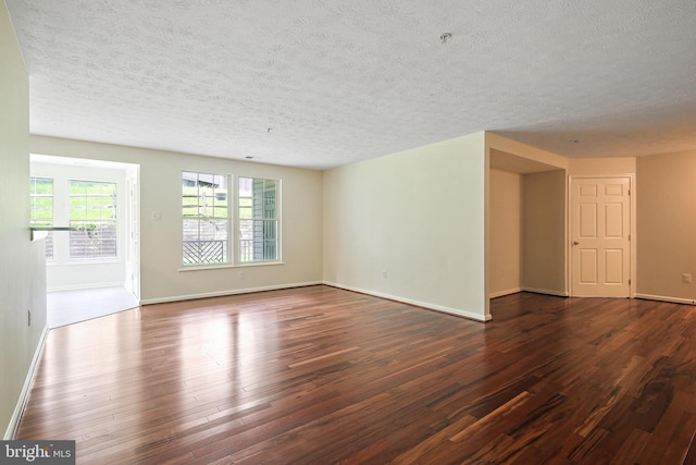 unfurnished living room with dark wood-type flooring, a textured ceiling, and baseboards