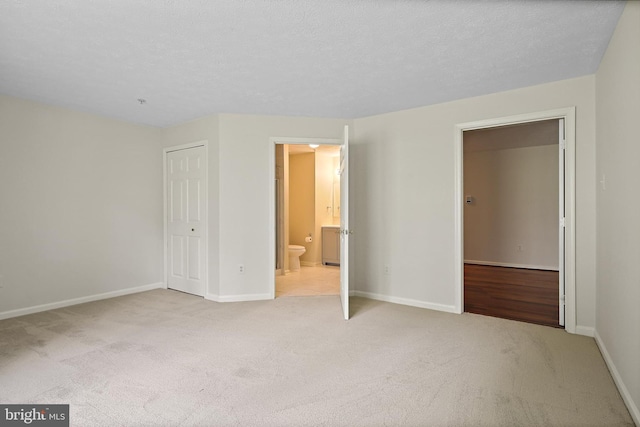unfurnished bedroom with light carpet, baseboards, and connected bathroom
