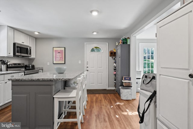 10317 Beaumont St, Fairfax, VA 22030 - kitchen featuring appliances with stainless steel finishes, white cabinetry, a center island, wood finished floors, and decorative backsplash