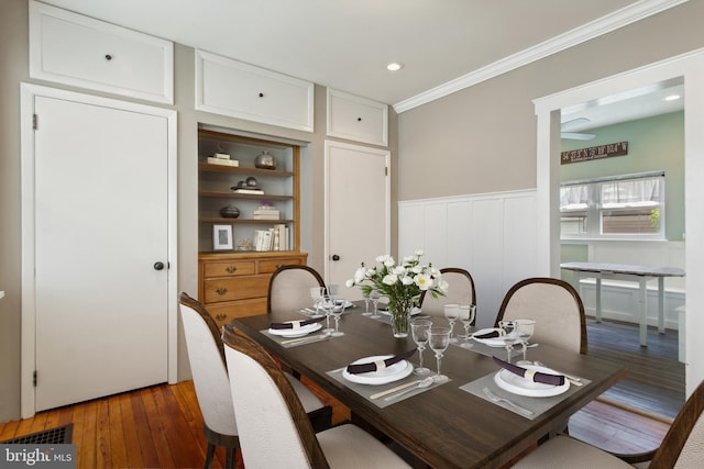 dining room featuring built in features, crown molding, a decorative wall, hardwood / wood-style floors, and wainscoting