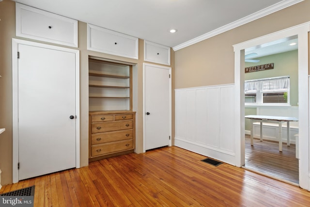 unfurnished bedroom featuring ornamental molding, light wood finished floors, a decorative wall, wainscoting, and recessed lighting