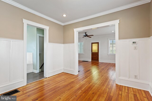 unfurnished room featuring light wood-type flooring, a decorative wall, ceiling fan, wainscoting, and crown molding