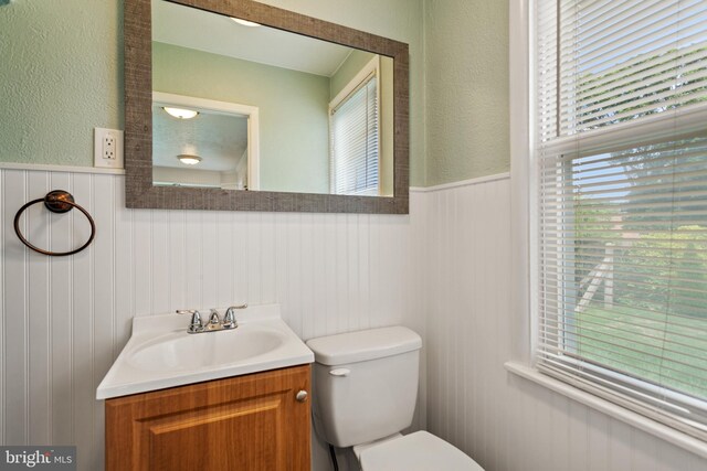 bathroom featuring a wainscoted wall, toilet, vanity, and a textured wall