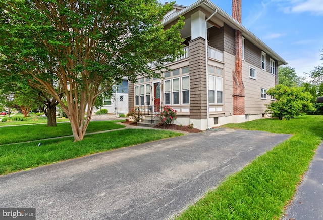 view of front of property featuring a chimney, a balcony, and a front yard