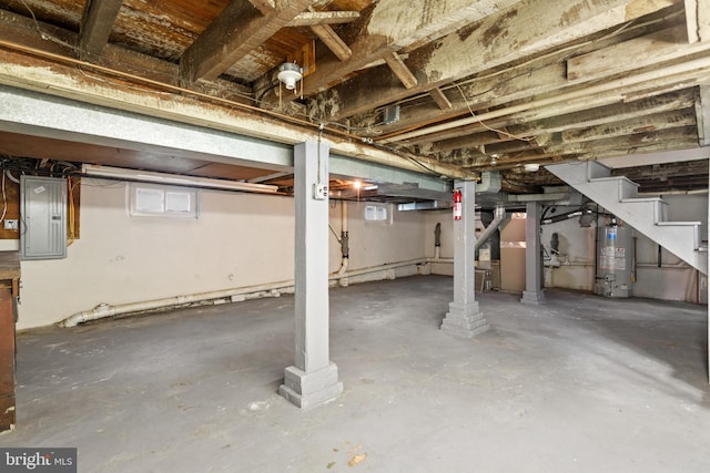 below grade area featuring water heater, electric panel, and stairs