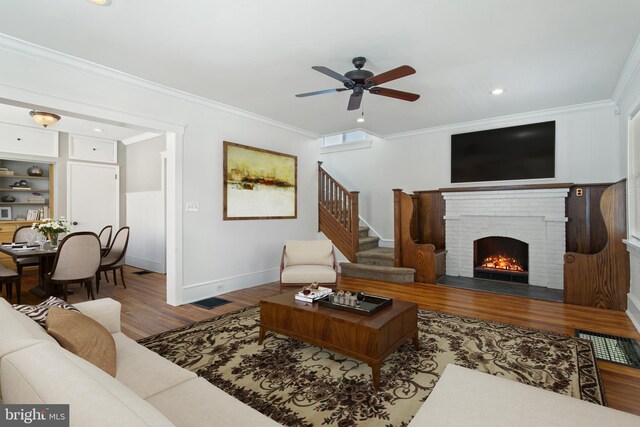 living room featuring wood finished floors, ceiling fan, crown molding, a fireplace, and stairs