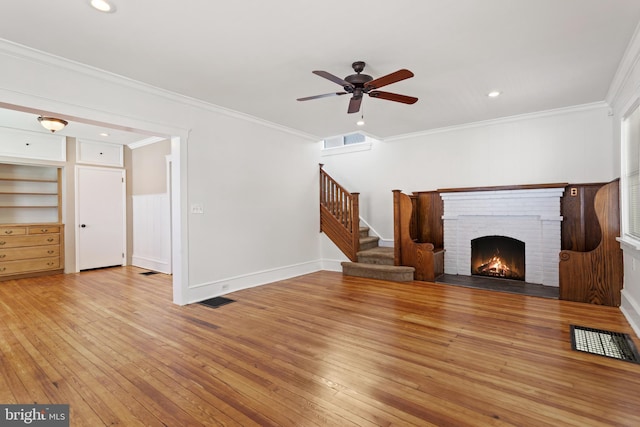 unfurnished living room featuring light wood-style flooring, stairway, a ceiling fan, a fireplace, and crown molding