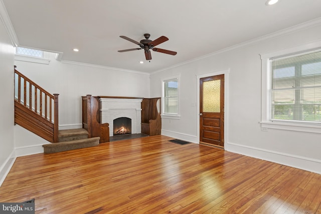 unfurnished living room featuring hardwood / wood-style flooring, stairway, a ceiling fan, ornamental molding, and baseboards