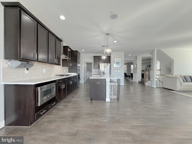 18030 Stump St, Dumfries, VA 22026 - kitchen featuring open floor plan, stainless steel appliances, a kitchen breakfast bar, dark brown cabinetry, and tasteful backsplash