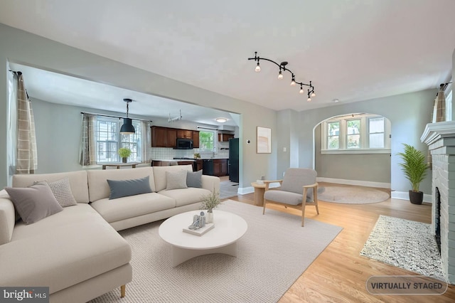 818 Glen Allen Dr, Baltimore, MD 21229 - living room featuring arched walkways, a brick fireplace, light wood-style flooring, baseboards, and track lighting