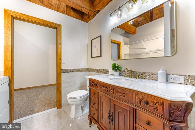 14854 Trout School Rd, Felton, PA 17322 - bathroom featuring toilet, vanity, tile walls, beamed ceiling, and a wainscoted wall