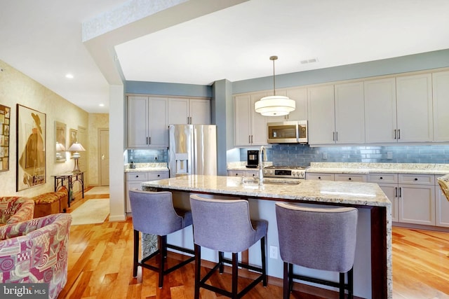 440 Belmont Bay Dr Unit 406, Woodbridge, VA 22191 - kitchen featuring appliances with stainless steel finishes, a sink, backsplash, light wood-style floors, and a kitchen breakfast bar
