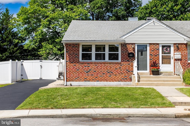 bungalow-style home featuring a gate, brick siding, and roof with shingles
