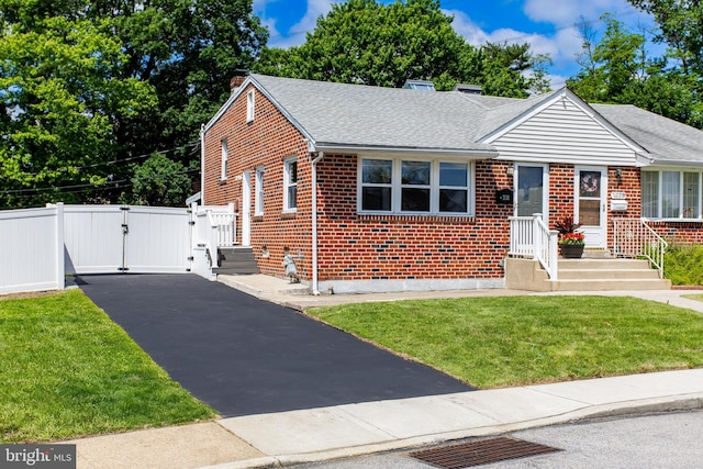 bungalow with a gate, brick siding, a shingled roof, a chimney, and asphalt driveway