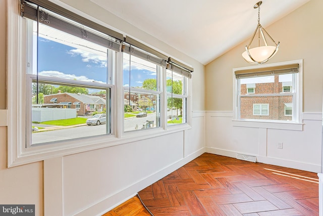 empty room featuring plenty of natural light, vaulted ceiling, and a wainscoted wall
