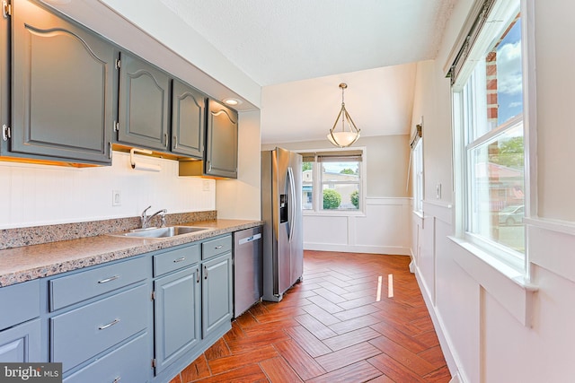 kitchen with stainless steel appliances, a sink, wainscoting, light countertops, and decorative light fixtures