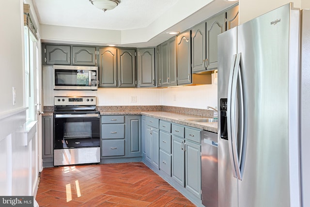 kitchen with appliances with stainless steel finishes, a sink, plenty of natural light, and gray cabinets