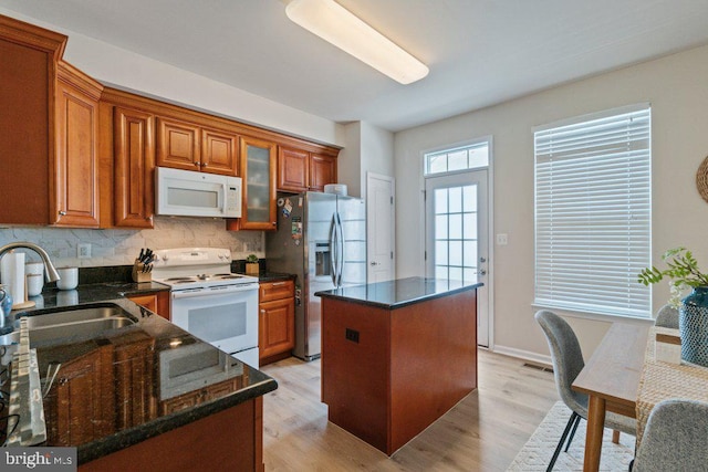 kitchen featuring white appliances, a center island, a sink, brown cabinets, and backsplash
