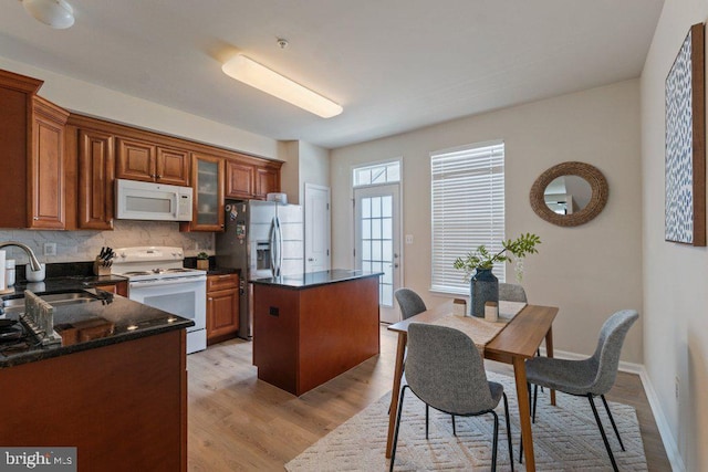 kitchen with white appliances, a sink, a kitchen island, decorative backsplash, and light wood-style floors
